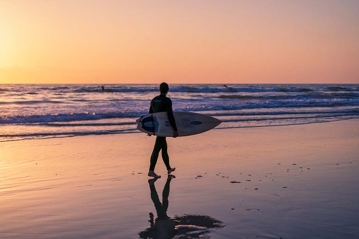 Mann mit Surfbrett am Strand im Urlaub