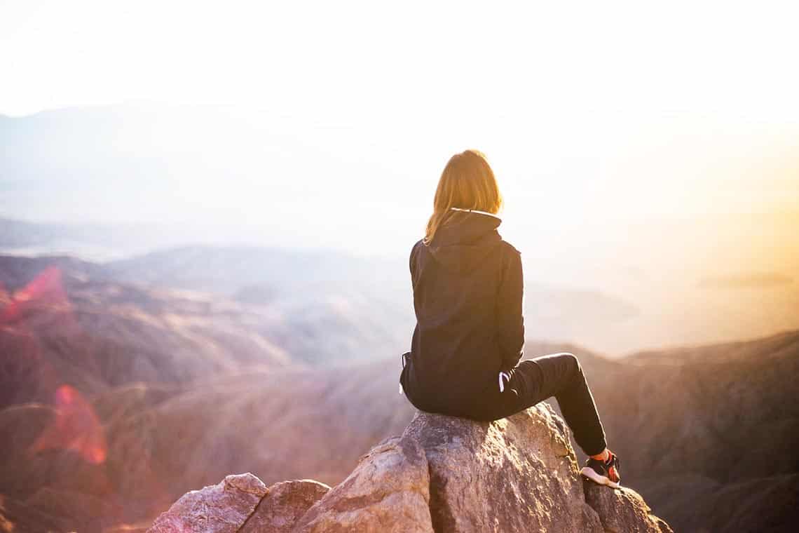 Frau sitzt auf einem Felsvorsprung auf einem Berg